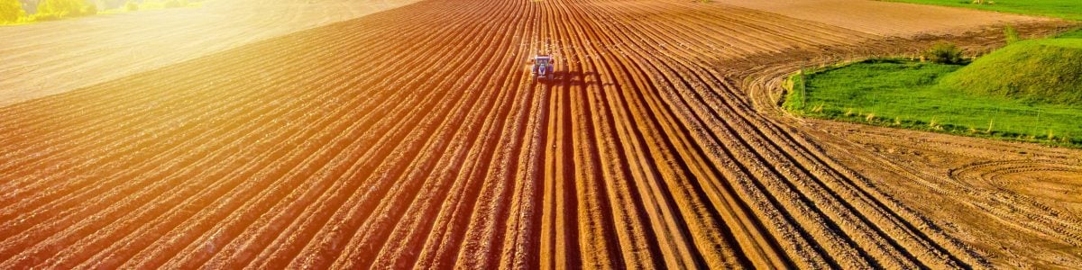 Farmer in tractor preparing land with seedbed cultivator in farmlands. Tractor plows a field. Agricultural work in processing, cultivation of land. Furrows row patter.aerial photo