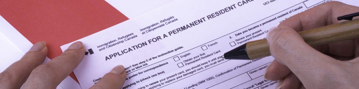 Filling Application (female hands and wood pen) form for Canadian Citizenship - Adults. Immigration, Refugees and Citizenship Canada on Canadian flag surface.