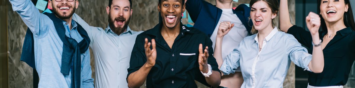 Young crew of happy excited male and female business partners celebrating completed startup project while looking at camera and laughing, overjoyed colleagues feeling amazed of done good work